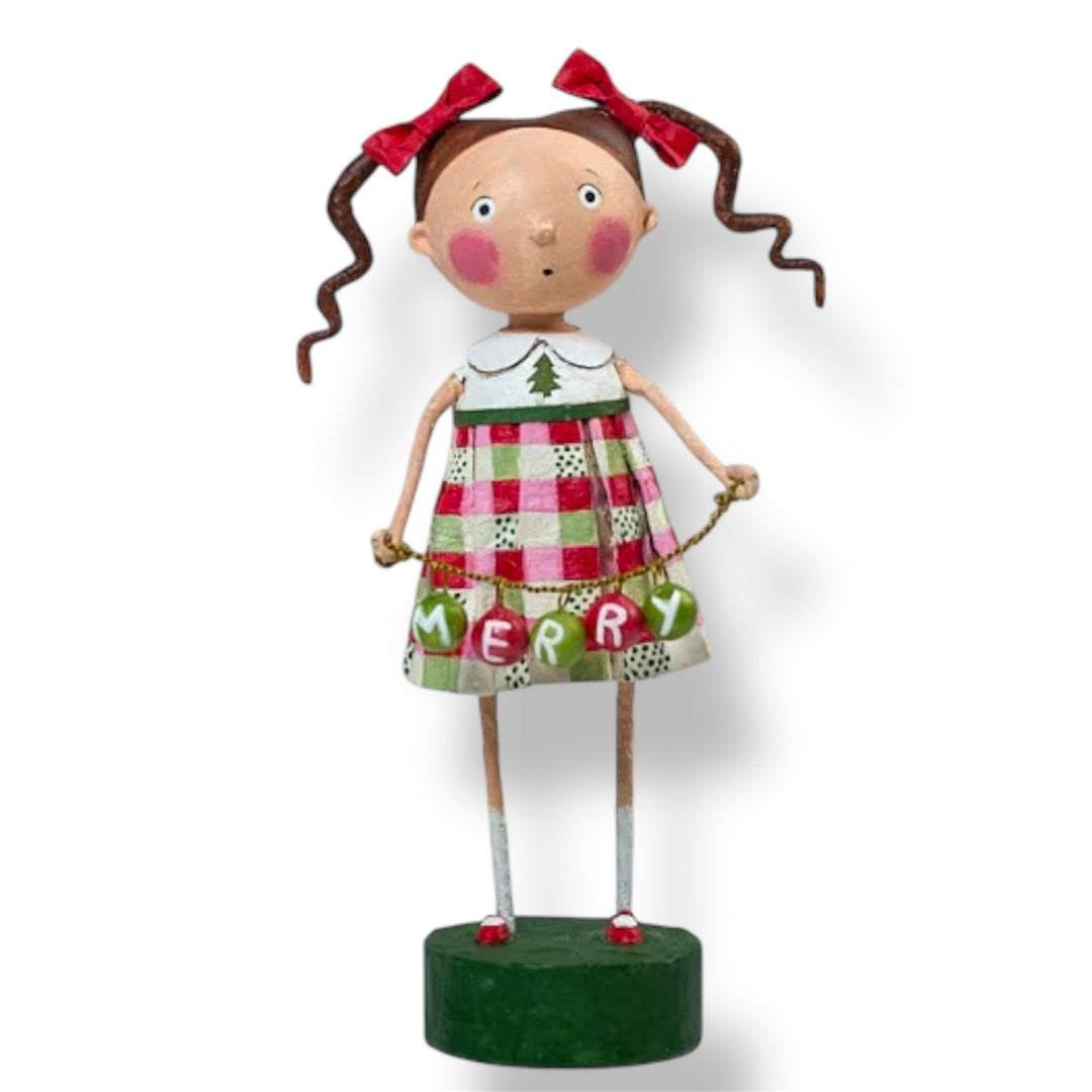 A Christmas figurine of a girl wearing a red and green plaid dress with the text 'MERRY' on it, standing on a green base.