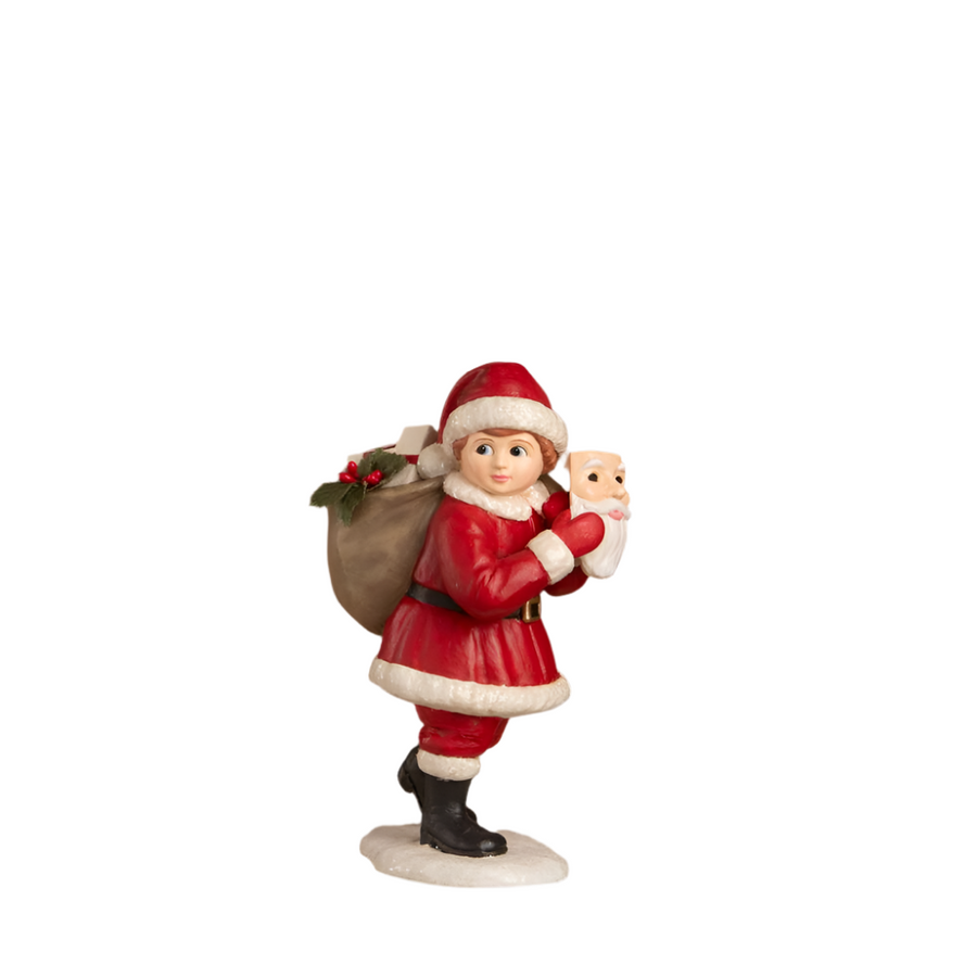 A hand-painted resin figurine of a boy dressed as Santa Claus, wearing a Santa face mask and carrying a sack of toys over his shoulder. The figurine is painted with attention to detail and has a touch of glitter, set against a plain background.