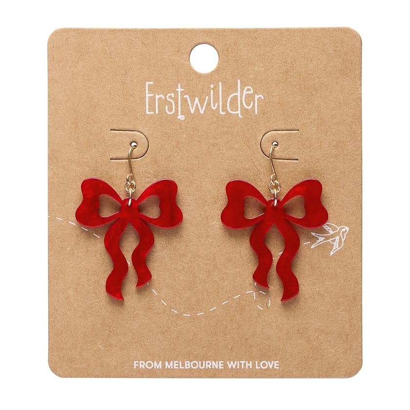 A pair of red bow-shaped dangle earrings on a brown kraft display card. The card has the brand name 'Erstwilder' printed at the top and 'FROM MELBOURNE WITH LOVE' at the bottom.