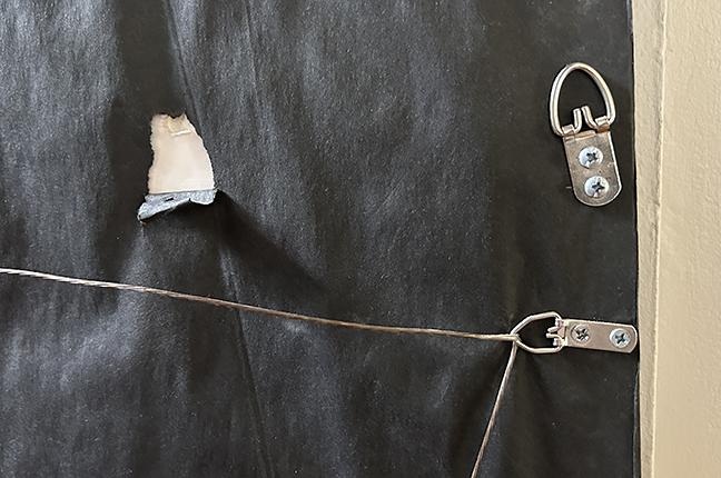 Detail of D-ring hanging hardware and small tear in the black dust cover on back of frame