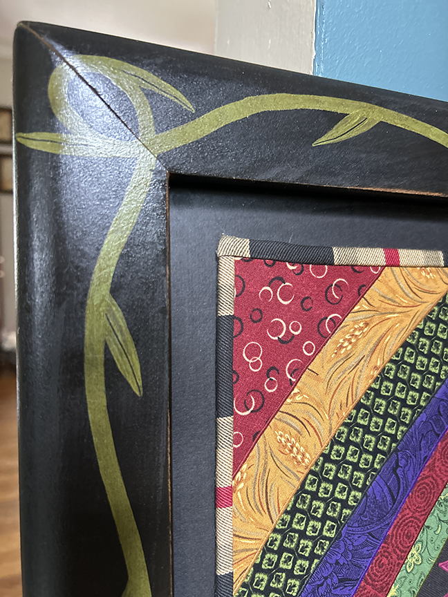 Corner of the hand-painted black wooden frame with green vine design and striped fabric binding, Chris Roberts-Antieau