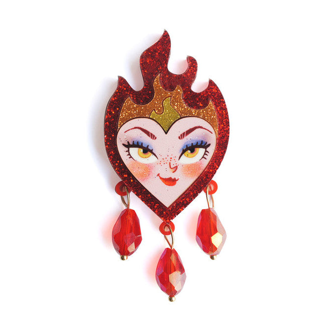 Heart-shaped brooch with face design, flames, and red dangling elements on a white background