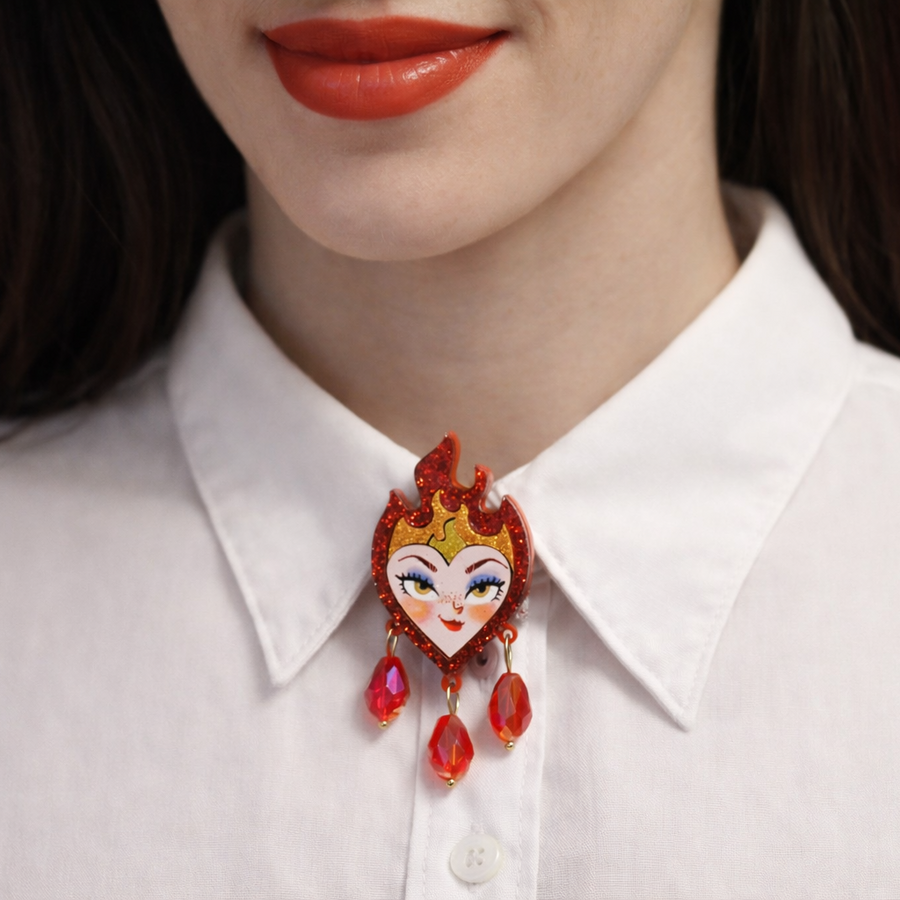 Close-up of a person wearing a white shirt with a decorative red and gold brooch.