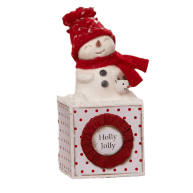 Decorative snowman figurine with red hat and scarf, sitting on a box with 'Holly Jolly' text.