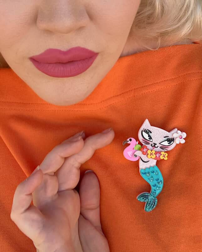 Person wearing an orange shirt with a decorative mermaid cat pin.